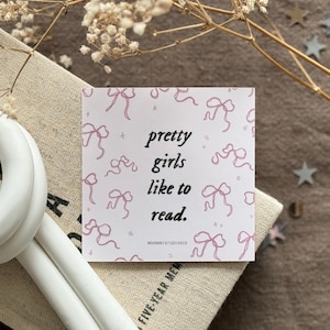 May include: A pink card with a white background and pink bows printed on it. The card has the text "pretty girls like to read." printed on it.