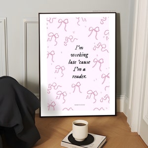 Op de afbeelding: Een roze printbare poster met een quote die luidt: "Ik werk laat omdat ik een lezer ben." De poster is versierd met roze linttekeningen.