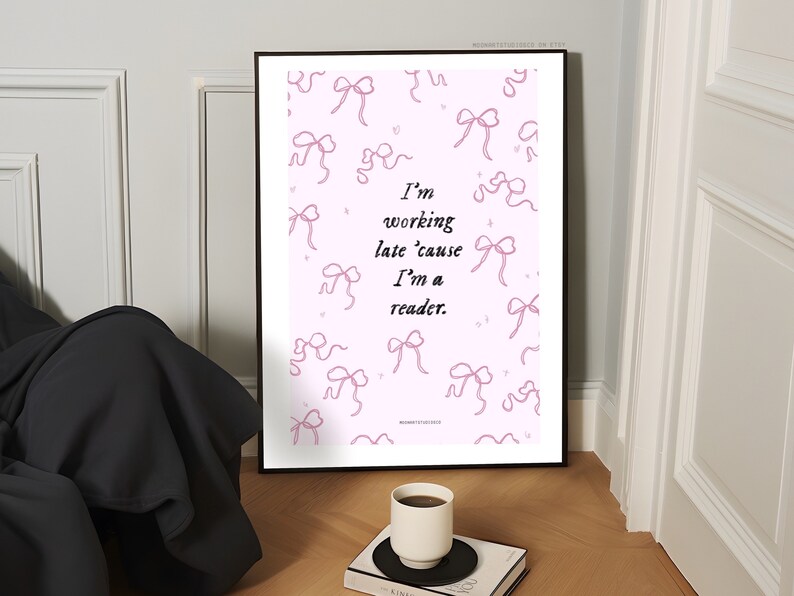 Op de afbeelding: Een roze printbare poster met een quote die luidt: "Ik werk laat omdat ik een lezer ben." De poster is versierd met roze linttekeningen.