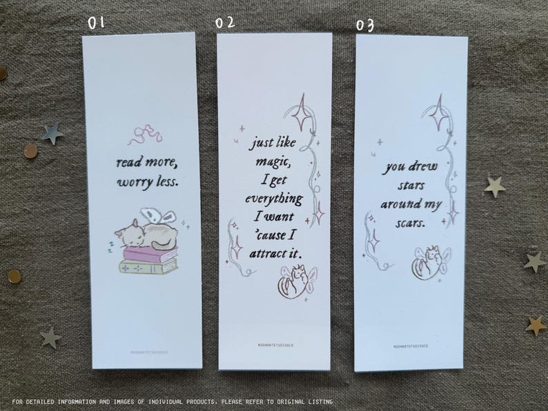Op de afbeelding: Drie witte bladwijzers met roze en grijze illustraties en tekst. De eerste bladwijzer toont een kat die slaapt op een stapel boeken met de tekst "lees meer, maak je minder zorgen." De tweede bladwijzer toont een kat met vleugels en de tekst "net als magie, krijg ik alles wat ik wil omdat ik het aantrek." De derde bladwijzer toont een kat met vleugels en de tekst "je hebt sterren getekend rond mijn littekens."