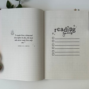 Puede incluir: Un cuaderno blanco cuadriculado con una cita sobre la lectura de George R.R. Martin en la p&aacute;gina izquierda y una lista de verificaci&oacute;n titulada "metas de lectura" en la p&aacute;gina derecha.