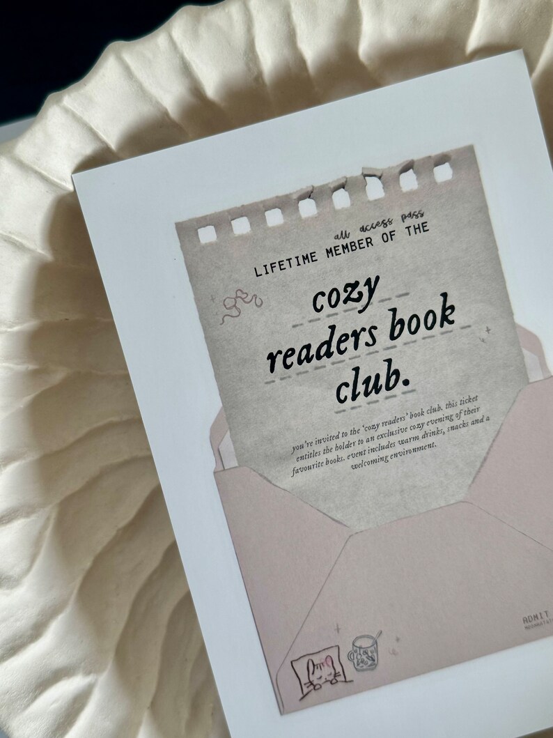 May include: A vintage-style ticket with a torn edge, reading "all access pass LIFETIME MEMBER OF THE cozy readers book club." The ticket is in a pink envelope with a hand-drawn illustration of a cat curled up with a mug.