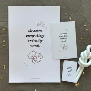 Może przedstawiać: Zestaw białych wydruków na papierze z napisem "she adores pretty things and witty words". Wydrukiom towarzyszy biały węzeł dekoracyjny. Wydruki zawierają ilustracje kopert i kokardek.