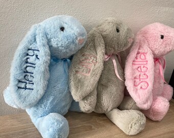May include: Three plush bunny toys with embroidered names. The blue bunny is named "Henry", the gray bunny is named "Lily", and the pink bunny is named "Stella".