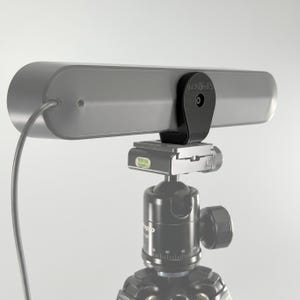 Può includere: Un dispositivo elettronico grigio, allungato e rettangolare con una staffa di montaggio nera fissata a una testa di treppiede. Il dispositivo presenta un cavo sottile che si estende dal lato sinistro e una piccola porta circolare. La testa del treppiede include una livella a bolla verde.