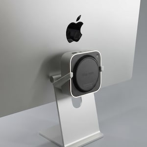 Peut inclure: Un ordinateur Apple iMac argenté avec le logo Apple noir au dos. Un Mac Mini carré et gris est monté à l'arrière de l'ordinateur. Le Mac Mini a un composant circulaire noir avec l'inscription "Mac mini".