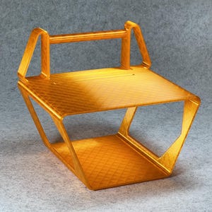 May include: A gold-colored plastic stand with a rectangular top and a curved bottom. The stand has a handle on the top and a grid pattern on the surface.