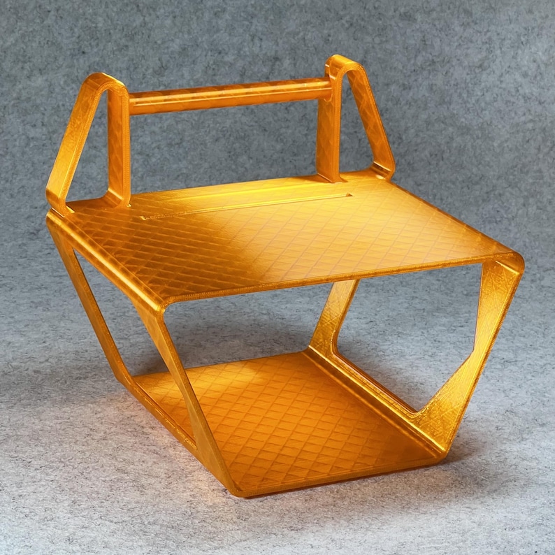 May include: A gold-colored plastic stand with a rectangular top and a curved bottom. The stand has a handle on the top and a grid pattern on the surface.