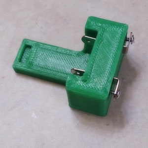 May include: Two green 3D printed battery holders with metal clips and screws. The holders are designed to hold two batteries side by side.