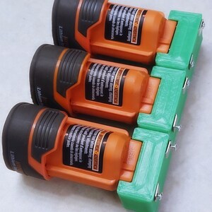 May include: Three orange and black lithium-ion batteries with green 3D printed battery holders. The holders have screws and metal plates to secure the batteries.