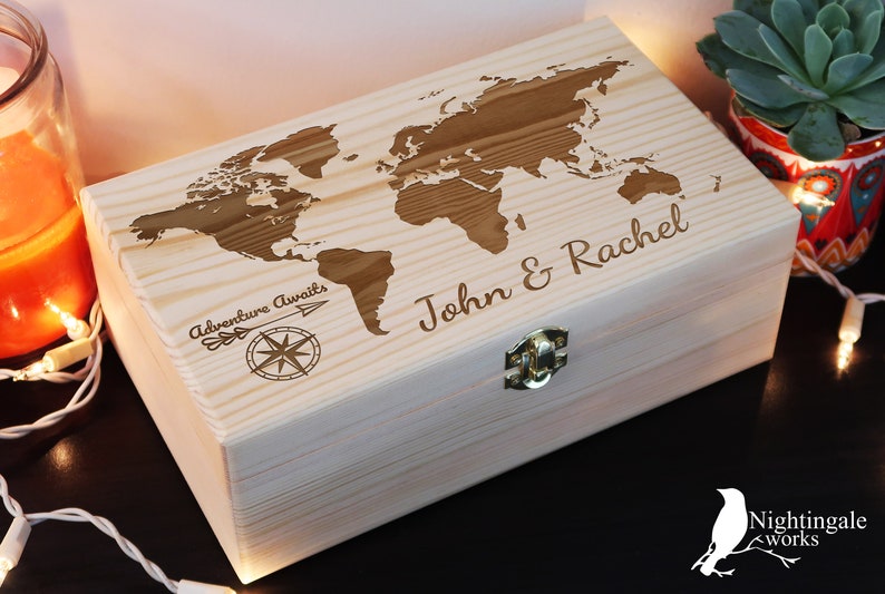 May include: A wooden box with a world map design and the text "Adventure Awaits" and "John & Rachel" engraved on the lid. The box has a brass latch.