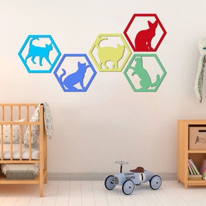 Pode incluir: Um conjunto de seis decora&ccedil;&otilde;es de parede hexagonais coloridas com recortes de silhuetas de gatos em v&aacute;rias poses. Os hex&aacute;gonos est&atilde;o dispostos em uma fila e s&atilde;o pintados em tons de azul, amarelo, verde e vermelho.