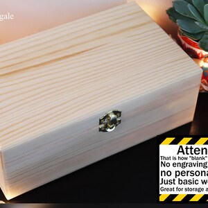 May include: A plain, unfinished wooden box with a brass latch. The box is closed and has a natural wood grain. The text "Attention! That is how "blank" option looks like No engraving, no names, no personalization. Just basic wooden box Great for storage and DIY projects" is printed on a yellow and black striped background.