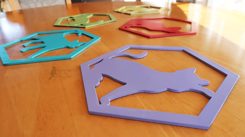 Pode incluir: Cinco pe&ccedil;as de decora&ccedil;&atilde;o de parede de madeira em forma de hex&aacute;gono com uma silhueta de gato recortada. Os hex&aacute;gonos s&atilde;o pintados em diferentes cores: azul-esverdeado, verde, amarelo, vermelho e roxo.