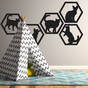 Pode incluir: Silhuetas de gatos pretos em molduras hexagonais numa parede cinza claro, com uma tenda tipi com padr&atilde;o de chevron preto e branco em primeiro plano.