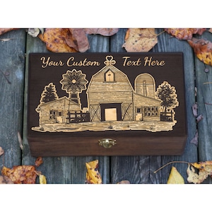 May include: A wooden box with a hinged lid and a metal latch. The box is decorated with a laser-engraved design of a farmhouse with a windmill, silo, and trees. The text "Your Custom Text Here" is engraved above the design.