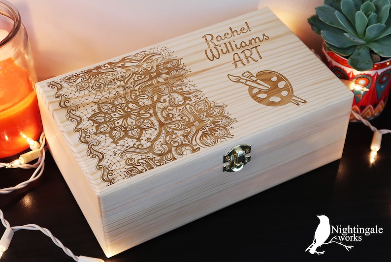May include: A wooden box with a personalized inscription that reads "Rachel Williams ART". The box is decorated with an intricate floral design and a paint palette with paintbrushes.