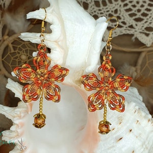 Könnte beinhalten: Ein Paar handgefertigte Ohrringe mit einem Blumenmuster aus braunem, orangefarbenem und goldenem Garn. Die Ohrringe haben unten eine Holzperle.