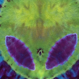 Pode incluir: T&ecirc;xtil tie-dye com um design sim&eacute;trico de rosto alien&iacute;gena. O rosto &eacute; predominantemente verde lim&atilde;o com grandes olhos roxos em forma de am&ecirc;ndoa. O fundo transita de azul para roxo e verde.