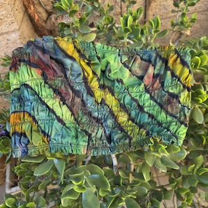 May include: A strapless tube top featuring a ruched, elasticized design with a tie-dye pattern in shades of lime green, yellow, teal, and dark brown. The garment has a gathered texture throughout and a straight hemline at the top and bottom edges.