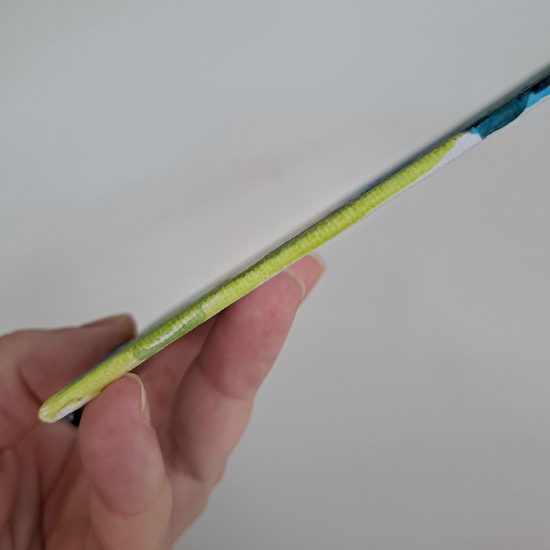May include: Close-up of the edge of a notebook with a green, blue and white watercolour design.