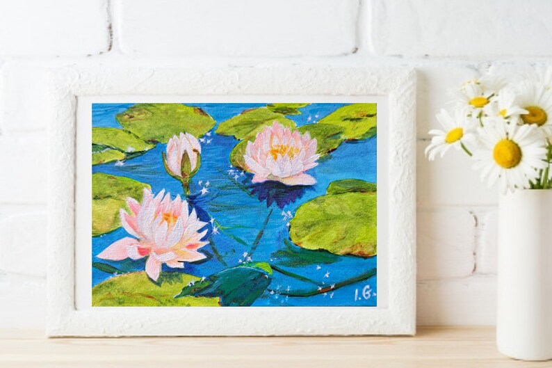 May include: A painting of pink water lilies with green lily pads on a blue background. The painting is framed in white.