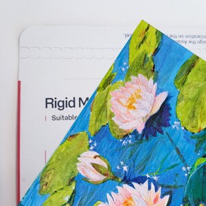 May include: A watercolour painting of white water lilies with green leaves on a blue background. The painting has a vintage feel and is perfect for a home decor project.