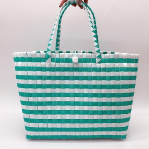 May include: A white and teal striped tote bag with two handles. The bag is made of woven plastic.