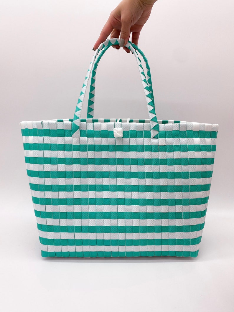 May include: A white and teal striped tote bag with two handles. The bag is made of woven plastic.