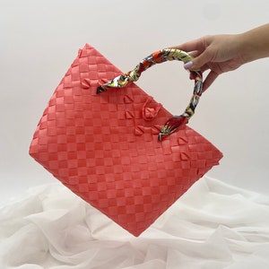 May include: A coral pink woven tote bag with a colorful patterned fabric handle.