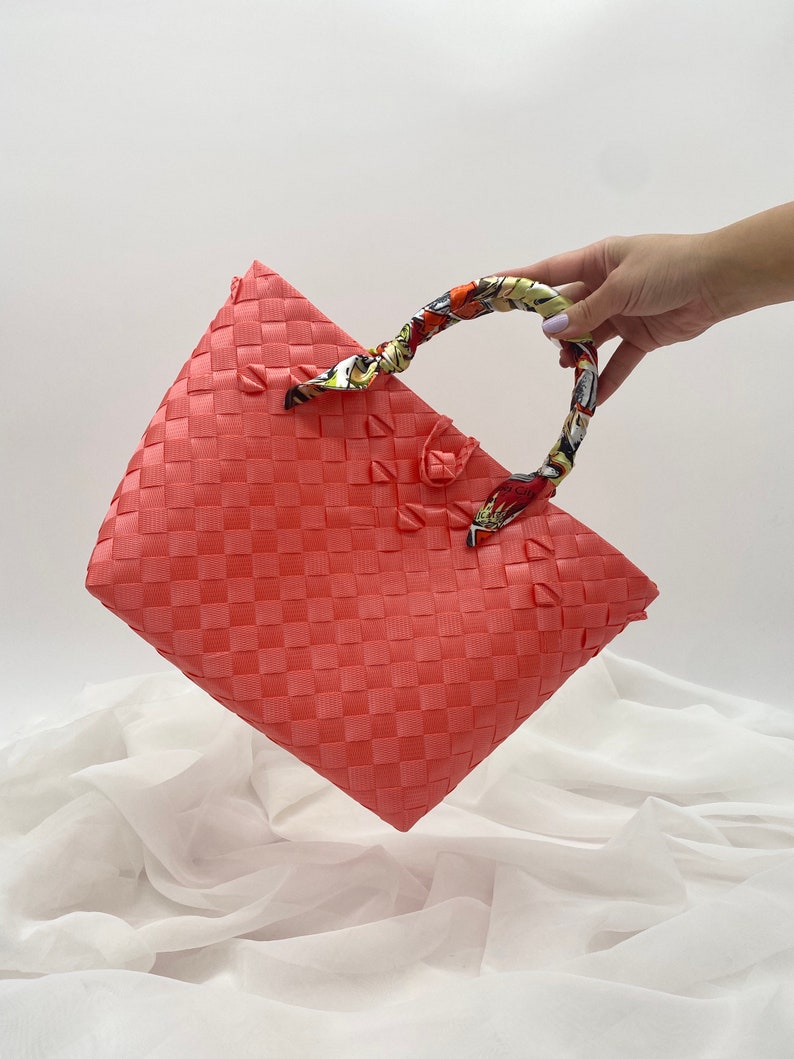 May include: A coral pink woven tote bag with a colorful patterned fabric handle.