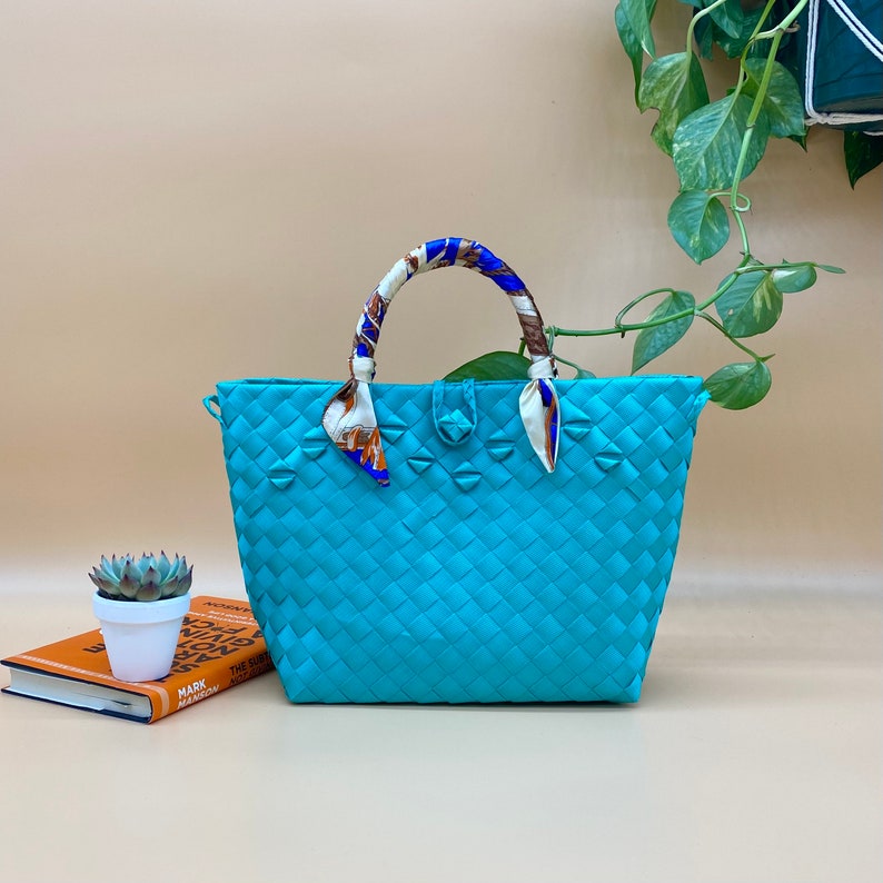 May include: A turquoise woven tote bag with a patterned fabric handle. The bag has a woven design and is made of a durable material.