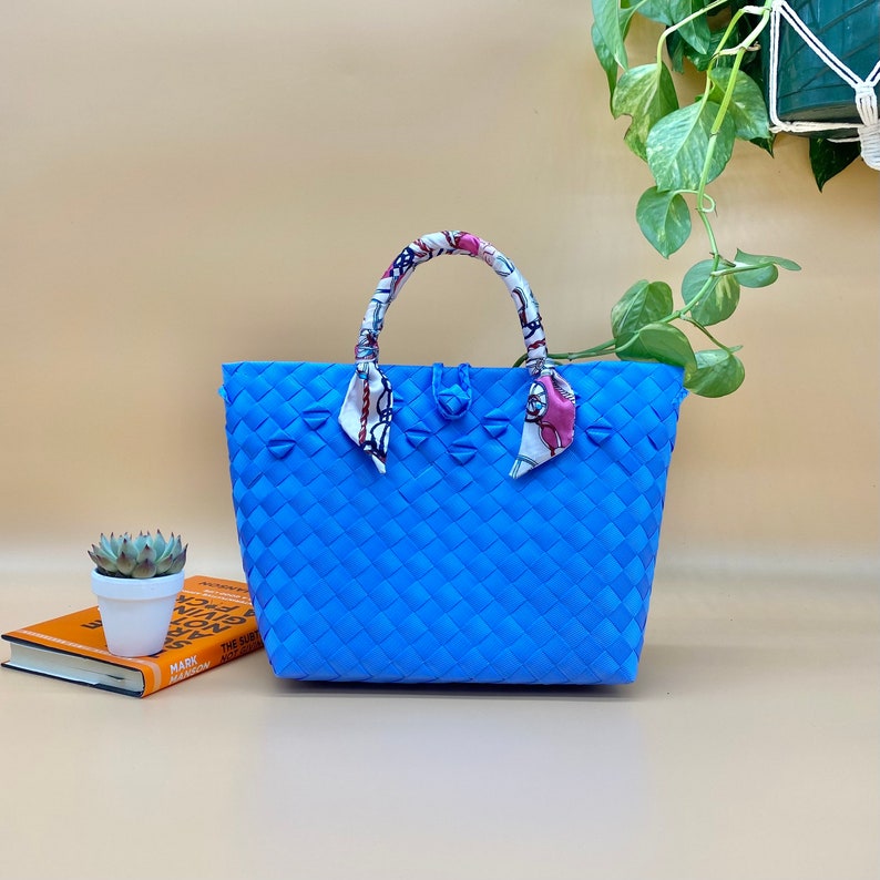 May include: A blue woven tote bag with a patterned fabric handle. The bag has a woven design and is made of a sturdy material.