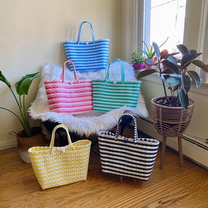 May include: Five striped tote bags in different colors, including blue, pink, green, black, and yellow. The bags are made of woven plastic and have a handle.