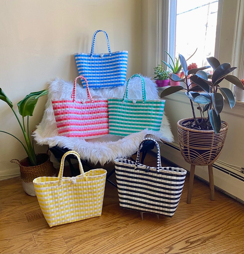 May include: Five striped tote bags in different colors, including blue, pink, green, black, and yellow. The bags are made of woven plastic and have a handle.