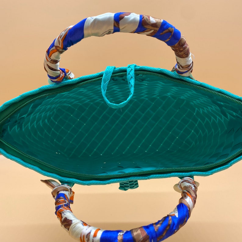 May include: A turquoise woven tote bag with a blue and white patterned fabric handle. The bag is open and the inside is visible.