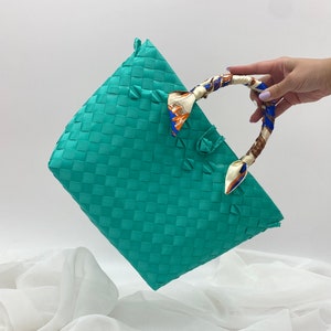 May include: A turquoise woven tote bag with a patterned fabric handle. The bag is made of a woven material and has a rectangular shape.