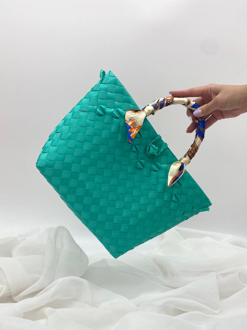May include: A turquoise woven tote bag with a patterned fabric handle. The bag is made of a woven material and has a rectangular shape.