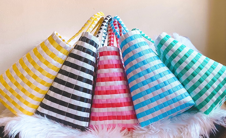 May include: Six colorful striped tote bags made of woven plastic. The bags are arranged in a pyramid shape with the yellow bag at the bottom and the green bag at the top. The bags are all different colors, including yellow, black, pink, blue, and green.