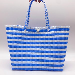 May include: A blue and white striped tote bag made of woven plastic. The bag has a single white button closure and two blue and white striped handles.