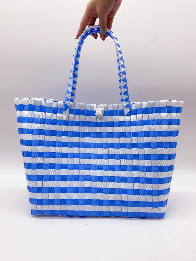 May include: A blue and white striped tote bag made of woven plastic. The bag has a single white button closure and two blue and white striped handles.