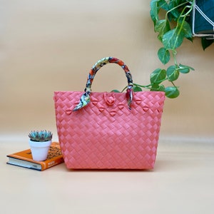 May include: A pink woven tote bag with a floral patterned fabric handle. The bag is made of a woven material and has a rectangular shape.