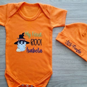 May include: Orange baby bodysuit and beanie set. The bodysuit features an embroidered ghost wearing a witch hat with the text "My First BOO!" and a name. The beanie says "Little Pumpkin". Perfect for Halloween.