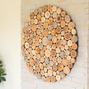 Op de afbeelding: Een cirkelvormig wandkunstwerk gemaakt van houten schijven in verschillende maten en tinten bruin, beige en grijs. De houten schijven zijn in een cirkelvormig patroon gerangschikt, wat een unieke en rustieke uitstraling creëert.