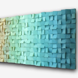 Op de afbeelding: Houten wandkunst met een kleurengradiënt. Het kunstwerk loopt over van lichtbeige naar tinten groen en blauw. Het oppervlak bestaat uit kleine, schuine houten blokken.