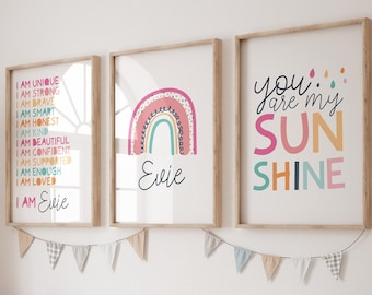 May include: Three framed prints with a rainbow and text. The first print has a rainbow with pink, orange, yellow, green, and blue colors. The text says "I am unique, I am strong, I am brave, I am smart, I am honest, I am kind, I am beautiful, I am confident, I am supported, I am enough, I am loved, I am Evie". The second print has a rainbow with pink, orange, yellow, green, and blue colors. The text says "Evie". The third print has text that says "You are my sunshine" in pink, orange, yellow, green, and blue colors.