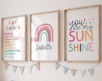 May include: Three framed prints with a rainbow theme. The first print features a rainbow with the name "Isabella" and positive affirmations. The second print features a rainbow with the name "Isabella". The third print features the text "You are my sunshine" in colorful letters.