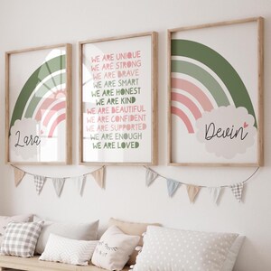 May include: Three framed prints with wooden frames. Each print features a rainbow design in shades of green and pink. One print has the name "Lara" in a cloud, another has the name "Devin". The center print has inspirational text.