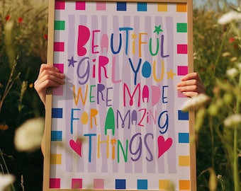 May include: A framed print with the words "BEAUTIFUL GIRL YOU WERE MADE FOR AMAZING THINGS" in colorful, playful lettering. The print has a light wood frame and is held in a field of tall grass and wildflowers.