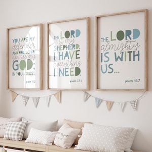 May include: Three framed wall art prints featuring religious text in blue and green typography. The prints display the phrases You are my defender, The Lord is my shepherd, and The Lord almighty is with us, each with a corresponding psalm citation.